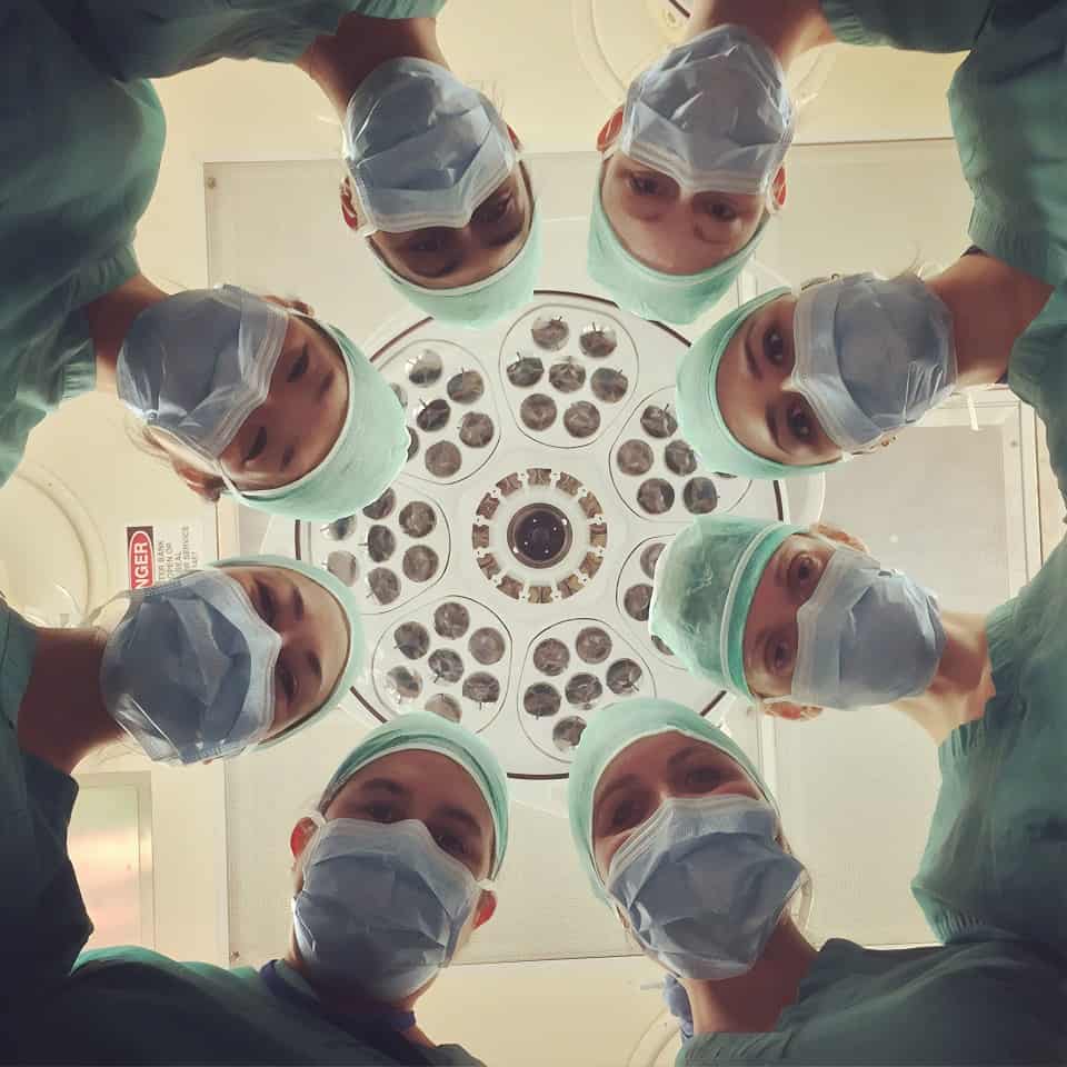 Eight surgeons gazing down on a patient in an operating room.