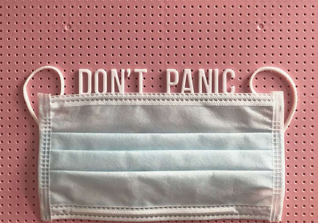 A surgical mask underlines the words "Don't Panic" spelled out in white plastic letters against a pink background.