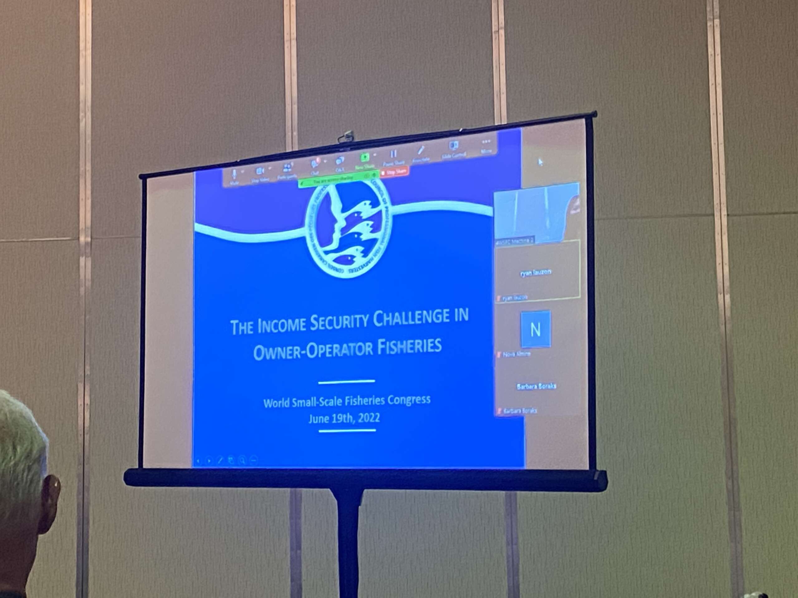 A projector screen with a presentation title slide that reads "The Income Security Challenge of Owner-Operator Fisheries."