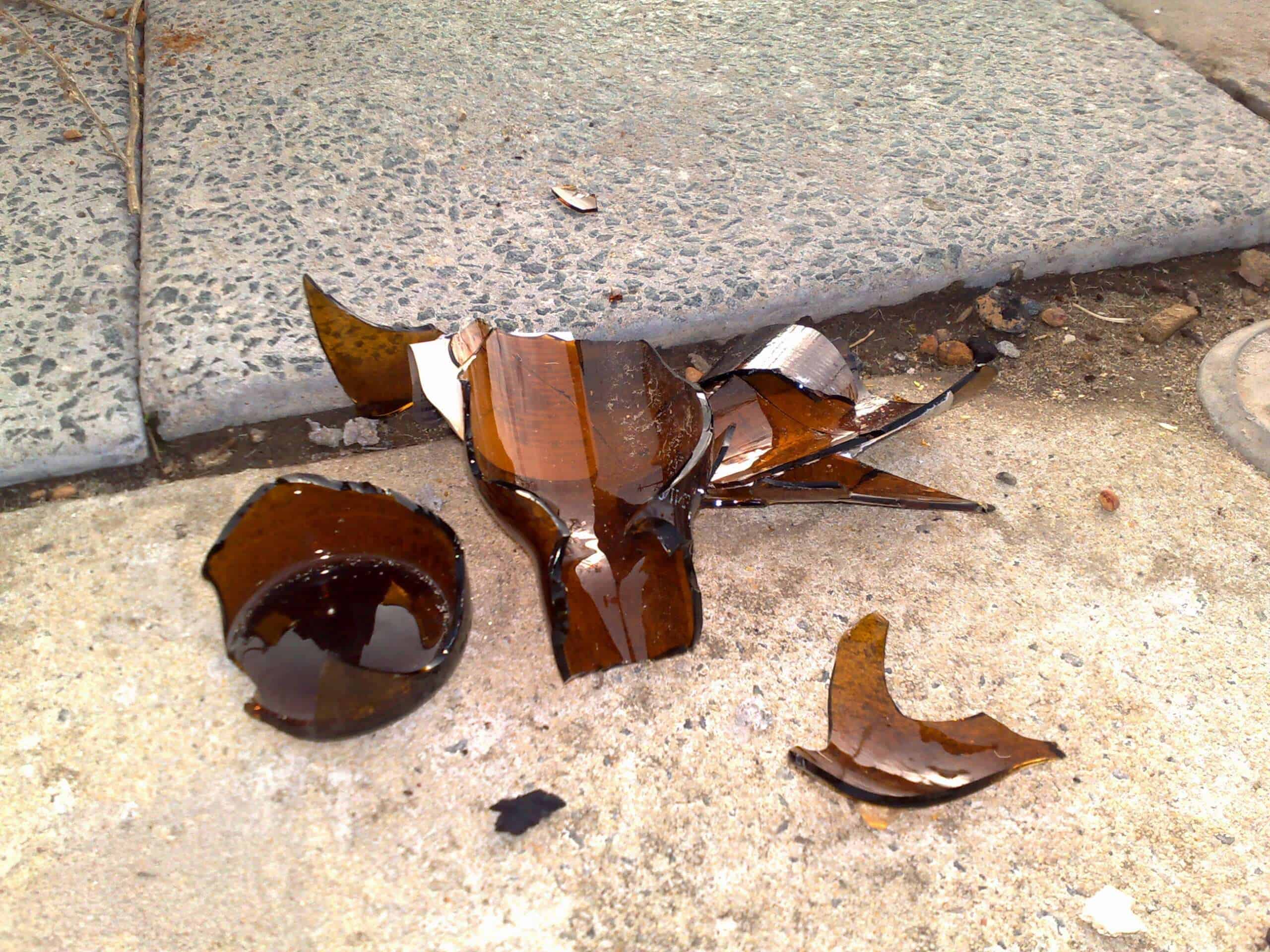 Broken beer bottle along a sidewalk curb.