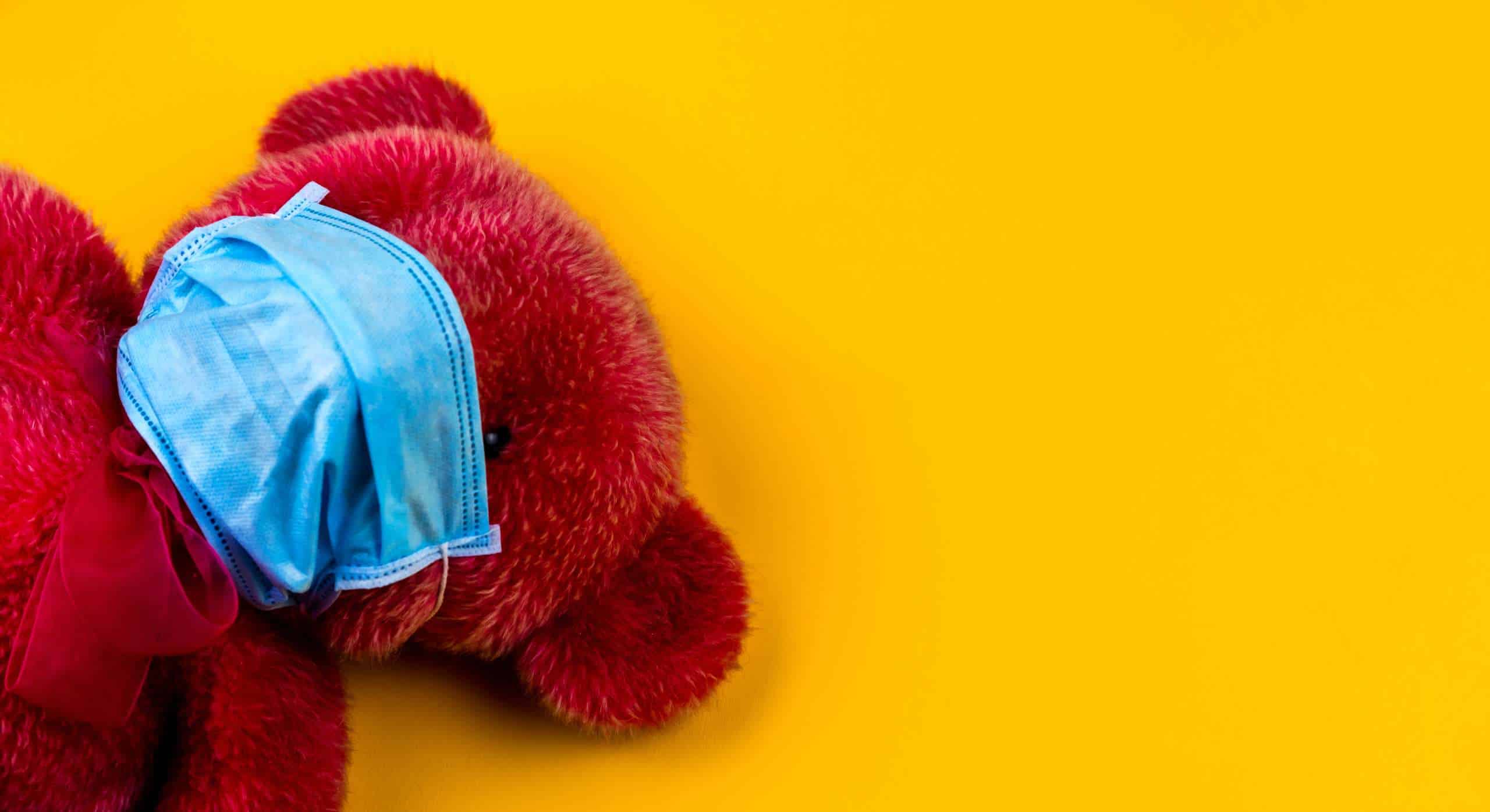 Lonely Red Teddy bear in a protective medical mask on a yellow background with respiratory mask.